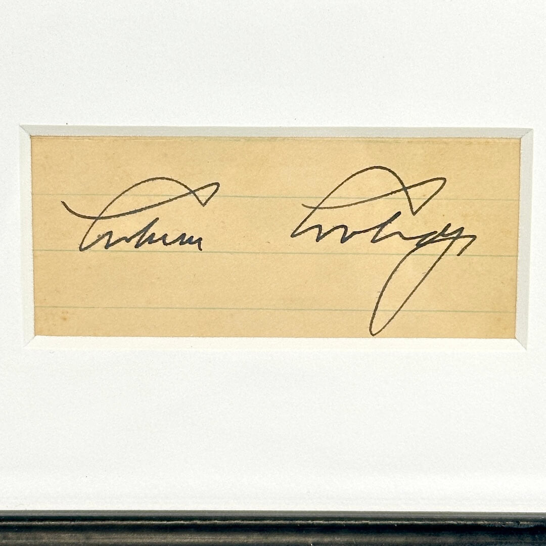 Close-up of black pen signature cut from lined paper, matted in frame. 