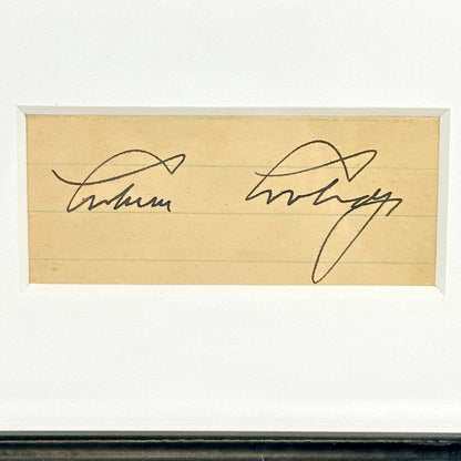 Close-up of black pen signature cut from lined paper, matted in frame. 