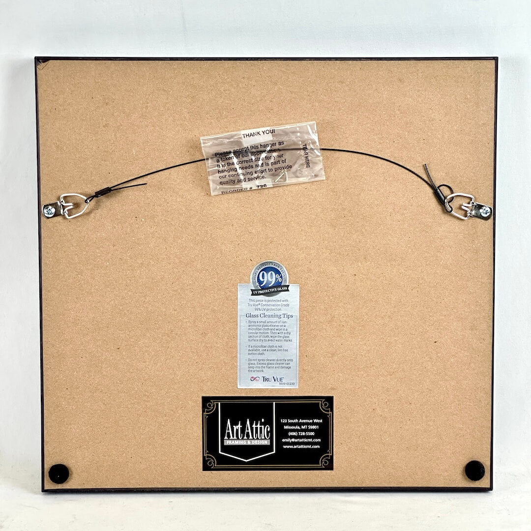 Backside of frame showing framer and care information, photographed against light background. 