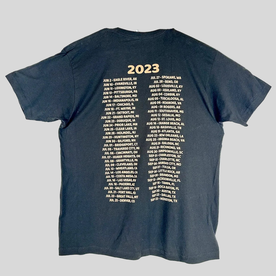A black t-shirt laid flat, showing the back side printed with '2023' in gold at the top, followed by two columns of gold text.