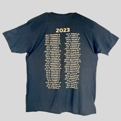 A black t-shirt laid flat, showing the back side printed with '2023' in gold at the top, followed by two columns of gold text.