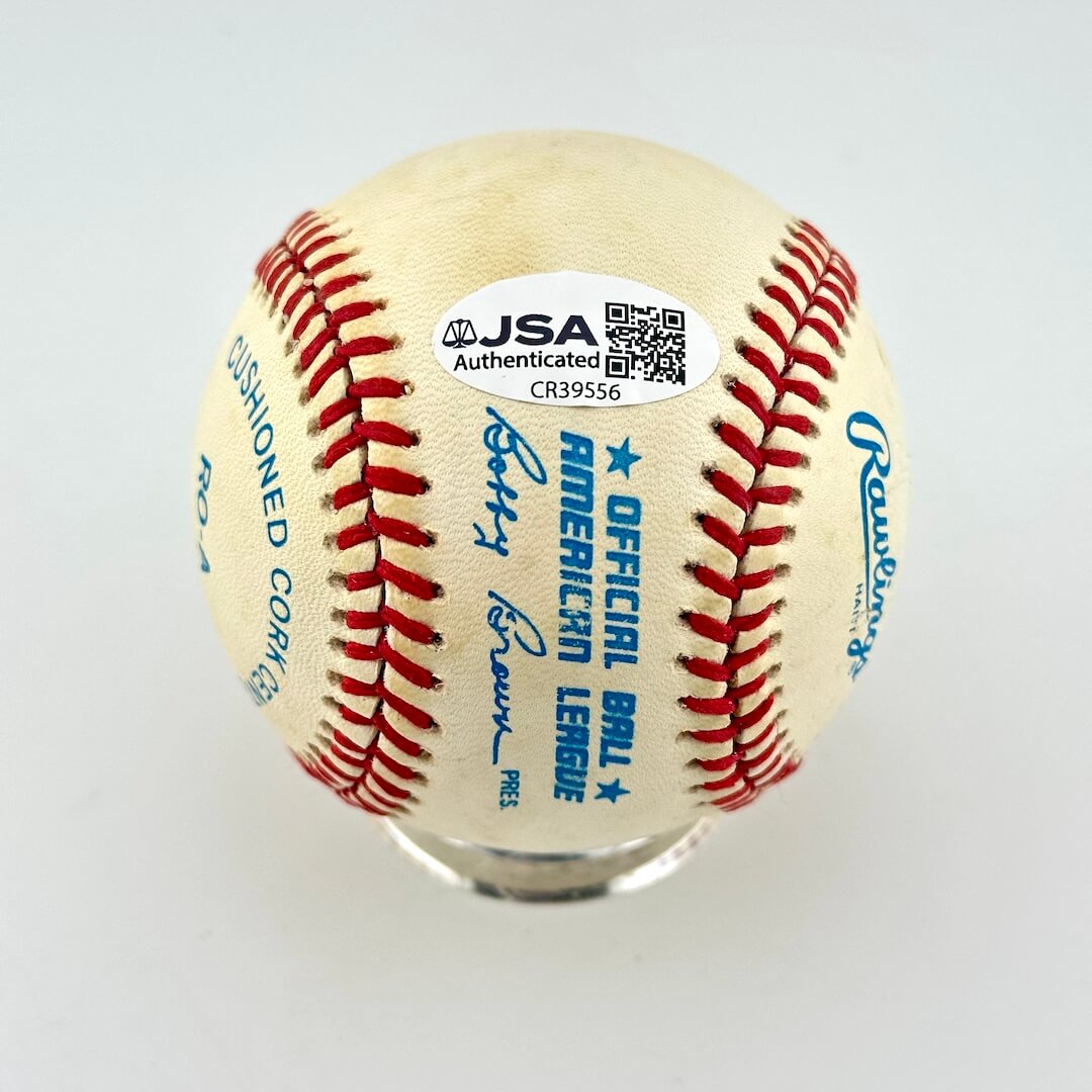 An official JSA authenticated baseball on a clear display stand, featuring red stitching, blue text, and authentication sticker.
