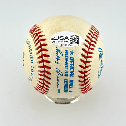 An official JSA authenticated baseball on a clear display stand, featuring red stitching, blue text, and authentication sticker.