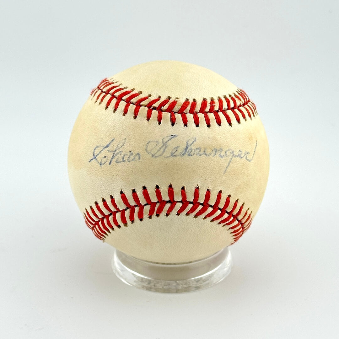 Baseball with red stitching on a clear stand against a white background