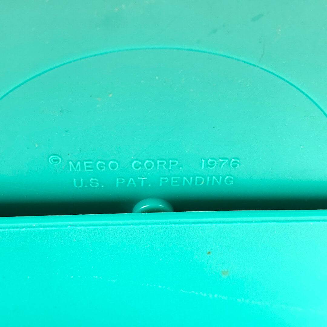 Close-up of a teal object with 'MEGO CORP 1976 U.S. PAT. PENDING' text.
