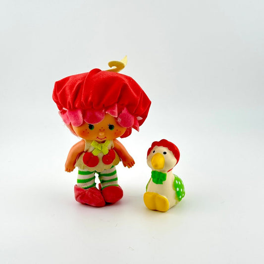 Two colorful toy figures, one with a red hat and the other  is a goose with a green outfit, on a white background.