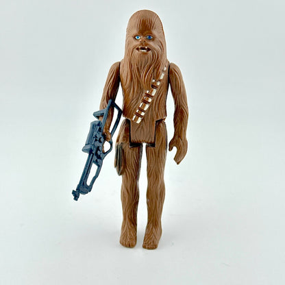 Action figure of a character with a brown textured body, holding a blue weapon on a white background