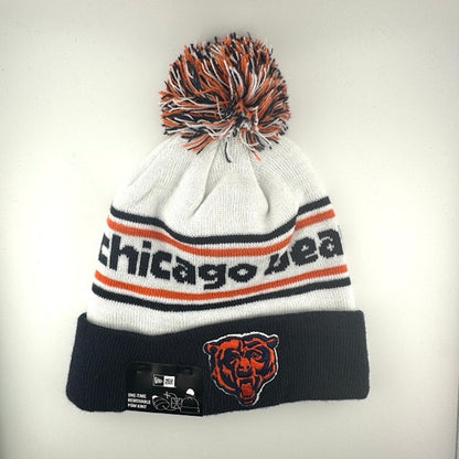 White knit cap with orange/navy stripes around navy text, navy cuff with Bears logo front center & navy/white/orange pom
