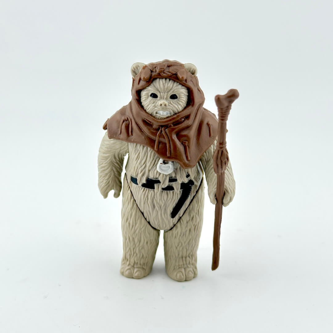 Toy figure of a character in a brown hood and beige outfit with a staff on a white background