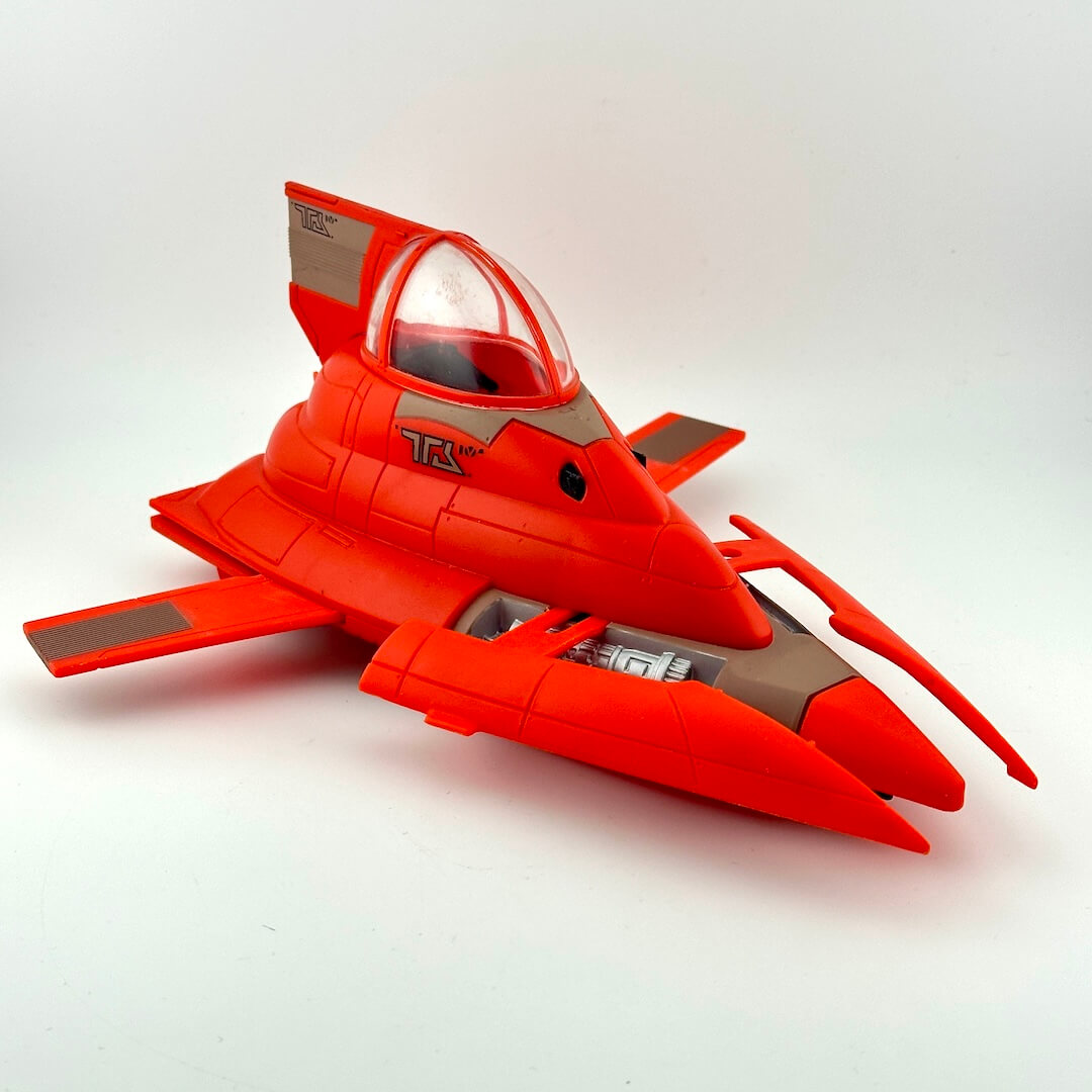A red toy spaceship with gray panels and a clear canopy, photographed on a plain light gray background.