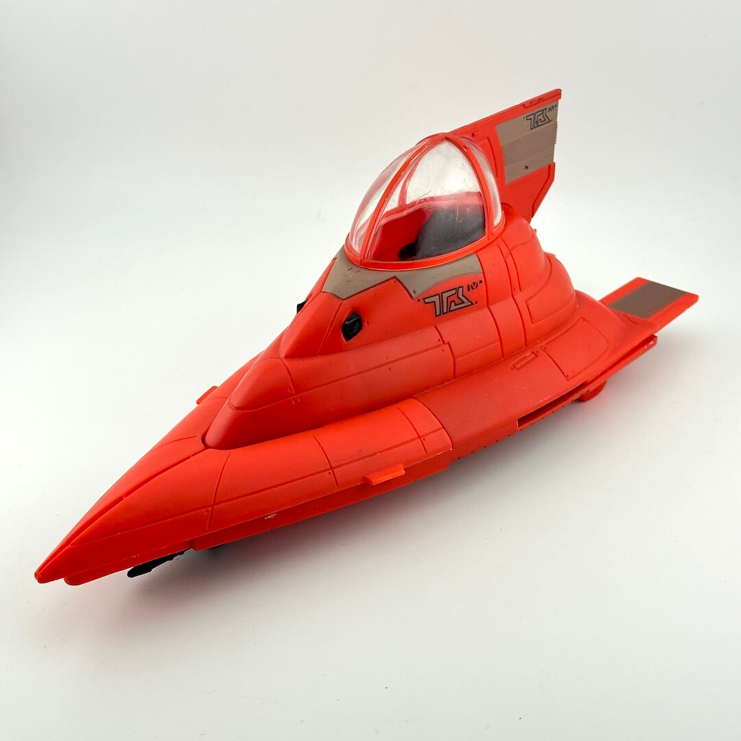 A red futuristic toy jet or spacecraft model with a clear canopy, photographed on a plain light gray studio background.