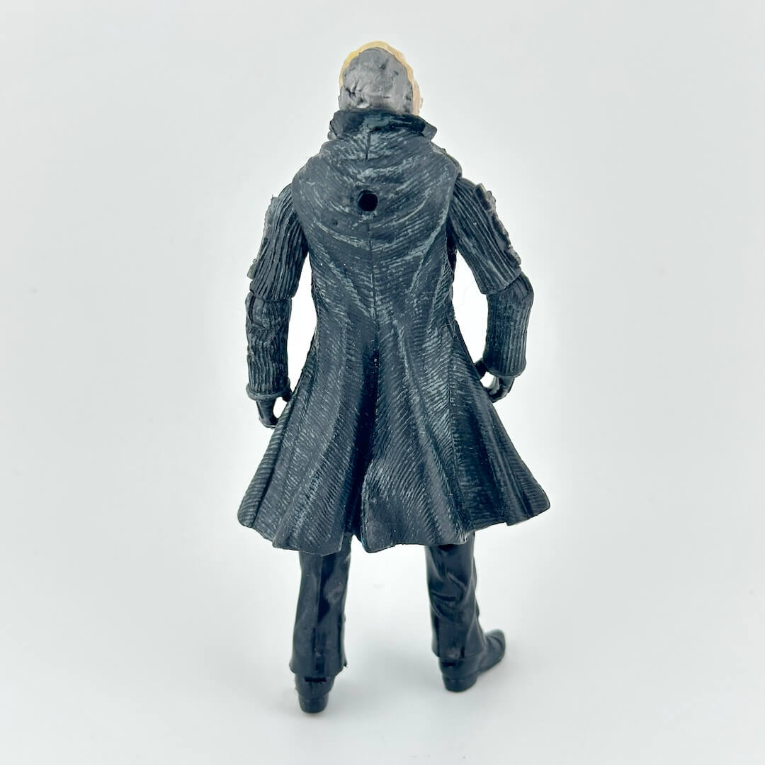 Back of action figure in long black coat and black pants with clear mask over head, against white background. 