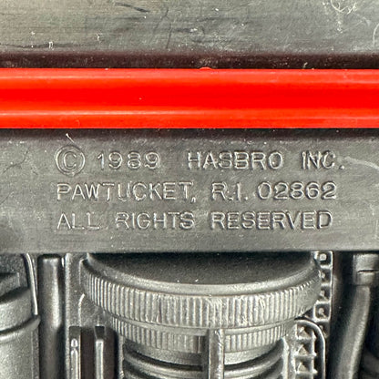 Close-up of a dark gray molded plastic component with embossed text reading '© 1989 HASBRO INC. PAWTUCKET, R.