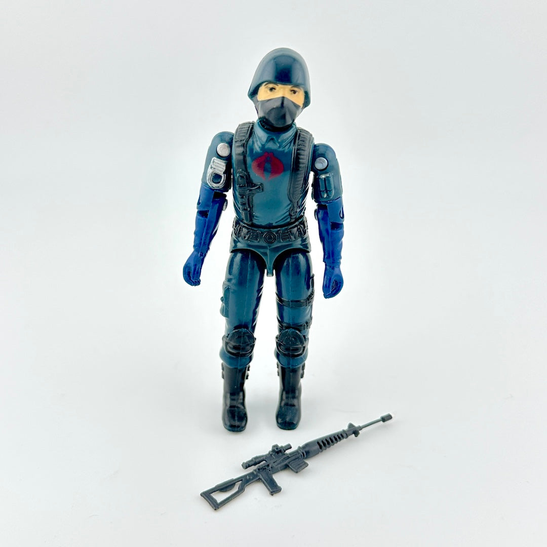 Action figure in blue outfit with gun accessory against white background. 