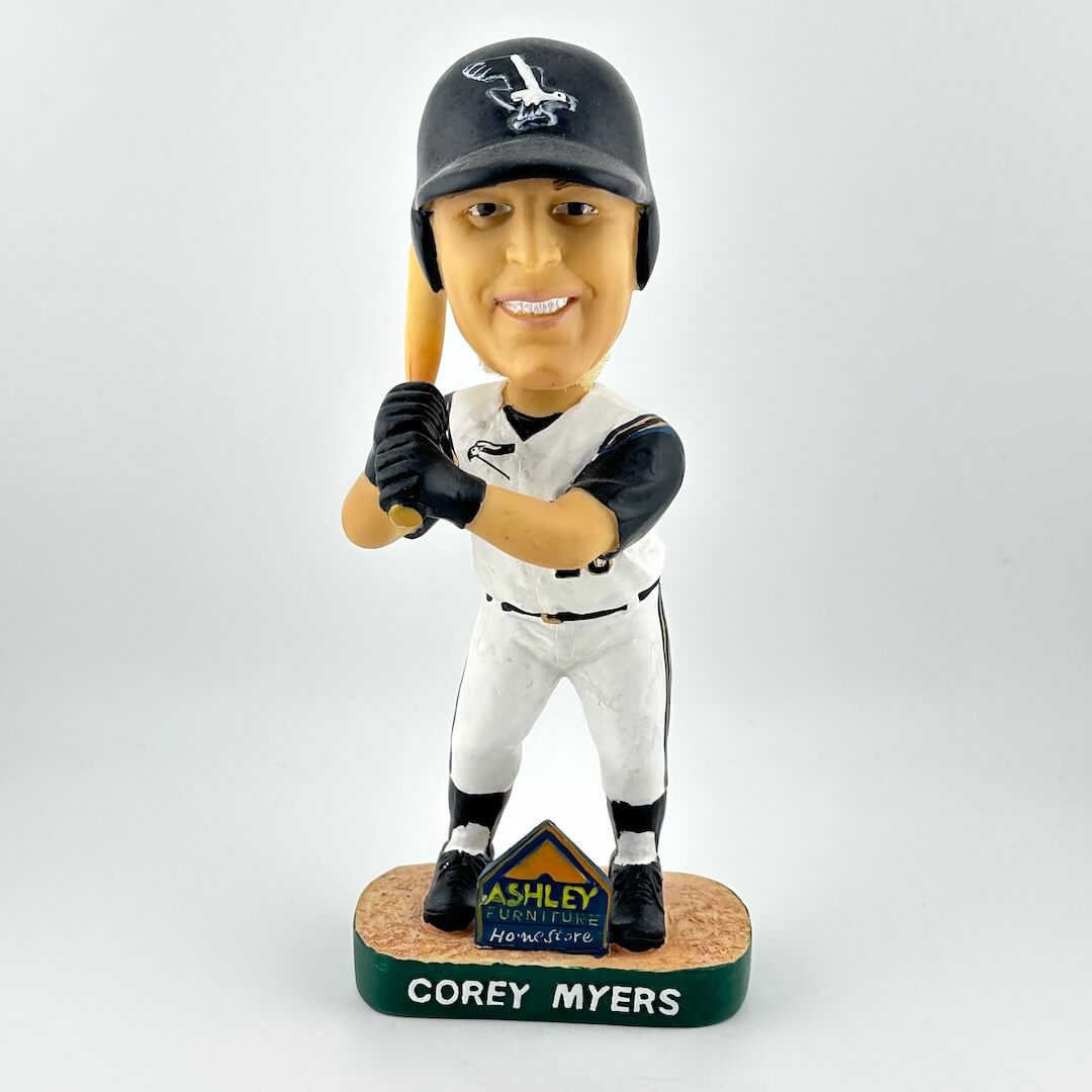 Baseball bobblehead figure of a player in a white uniform with a black helmet and bat, on a light gray background.