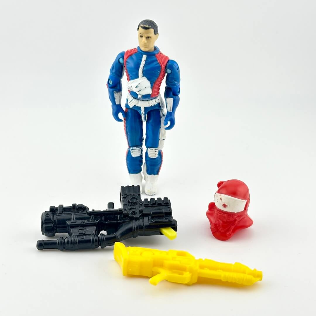 GI Joe action figure in blue flight suit with  multicolored accessories photographed on a white background. 