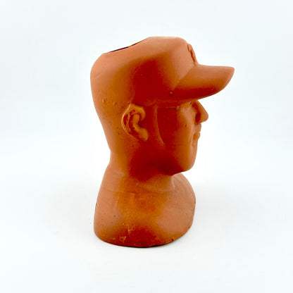 Terracotta sculpture of a man's head wearing a baseball cap on a white background
