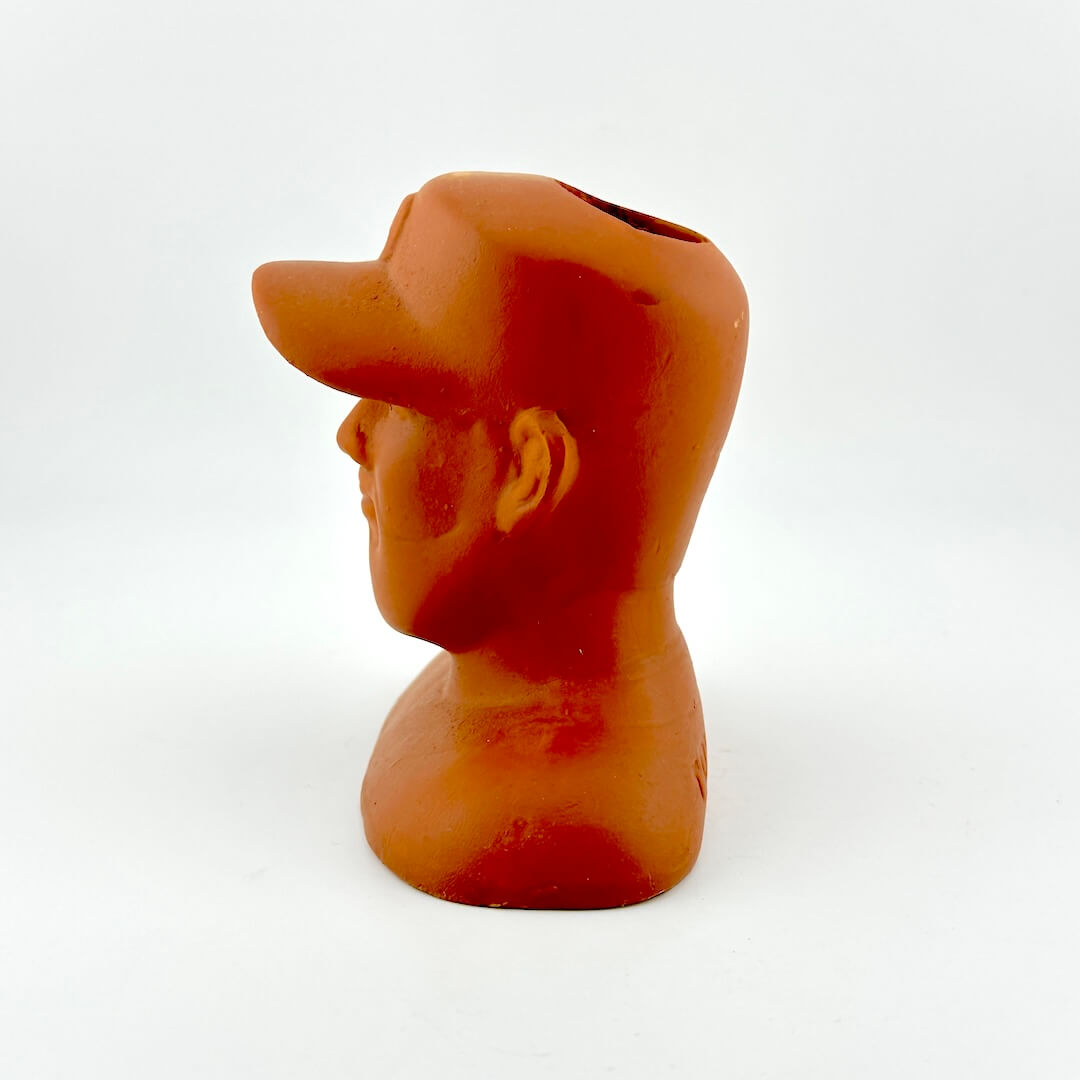 Terracotta sculpture of a man's head wearing a baseball cap on a white background