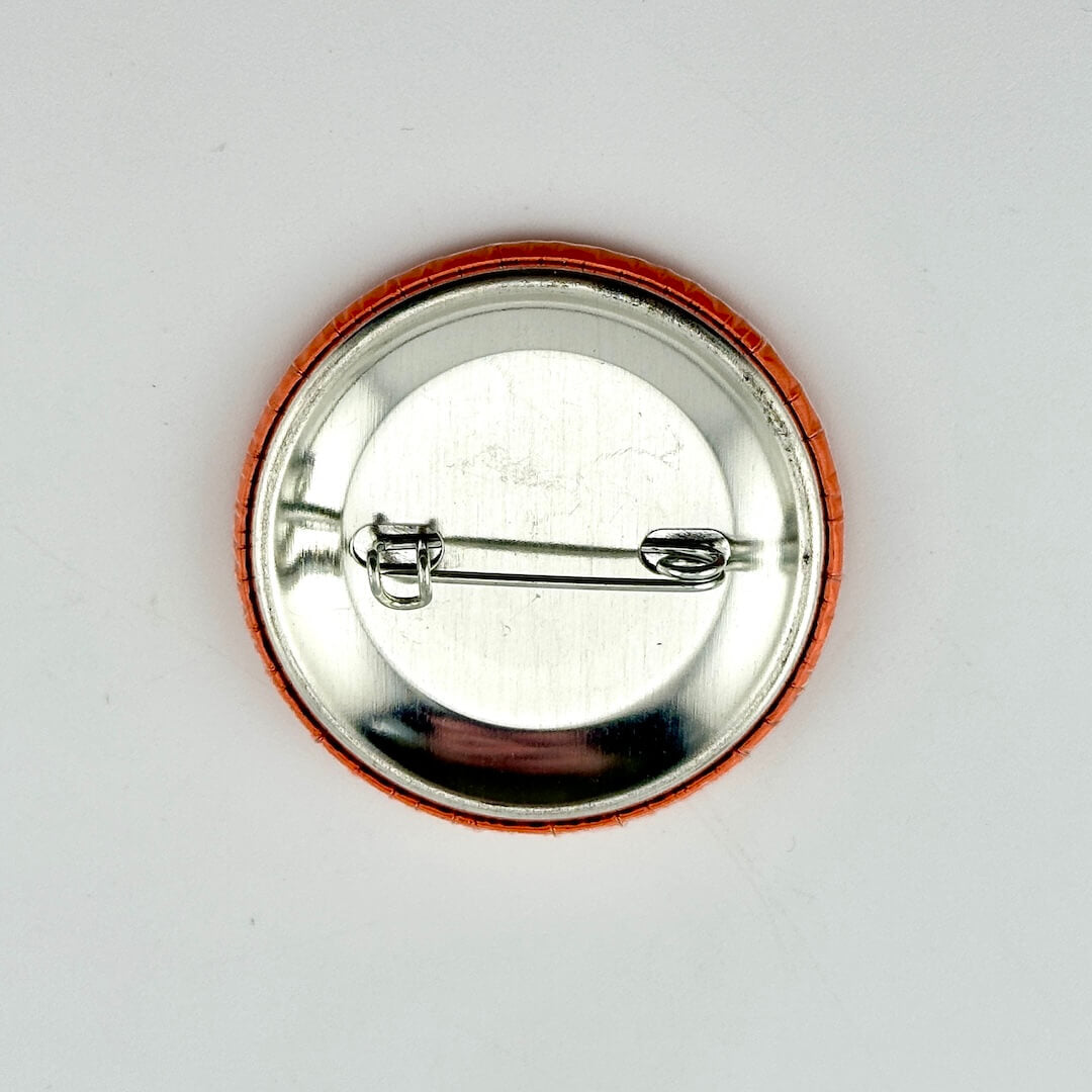 Round metal badge with a pin on a white background
