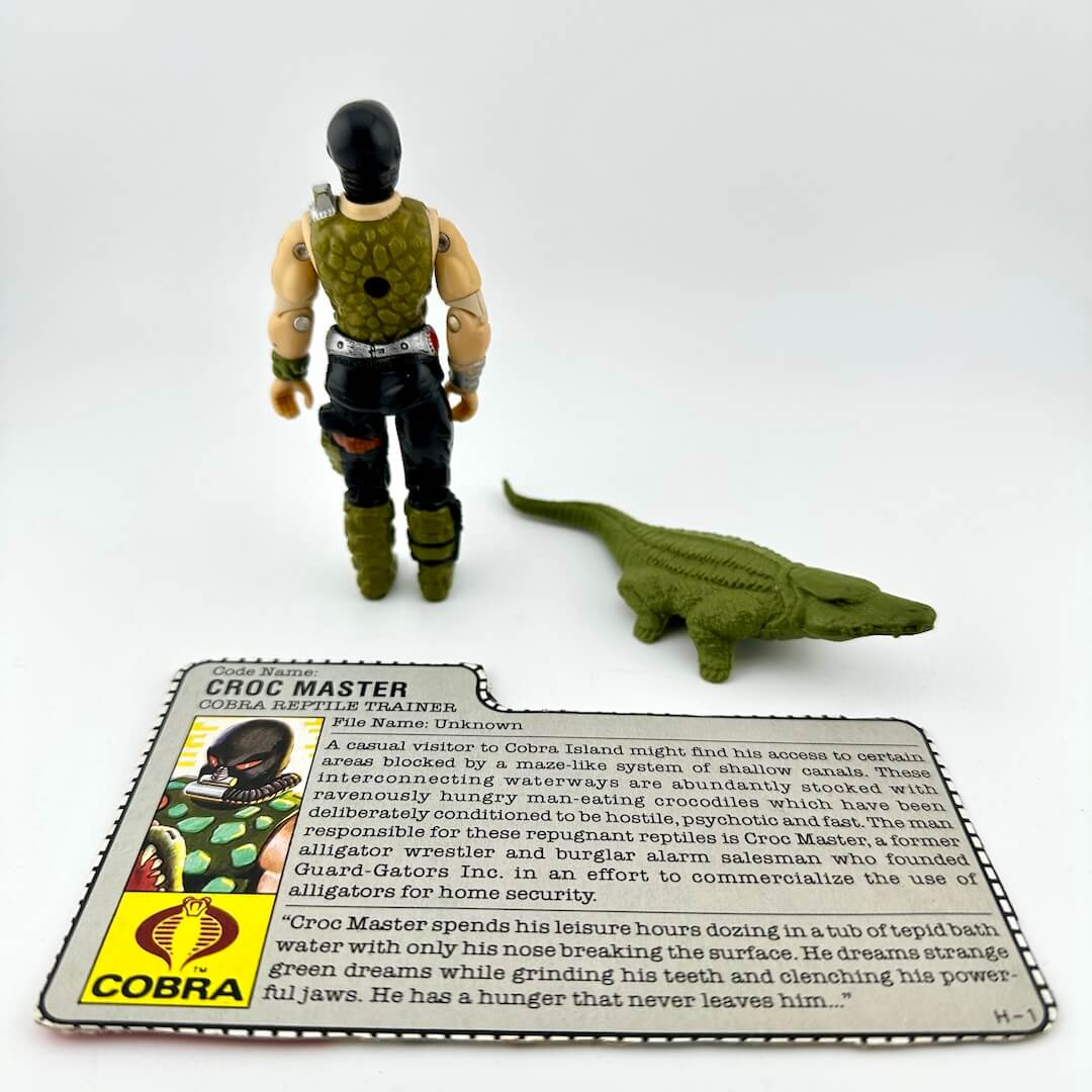 Toy figure of a crocodile and a person with a card labeled 'Croc Master' on a white background