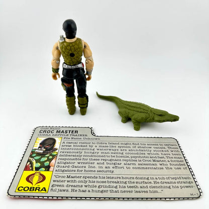 Toy figure of a crocodile and a person with a card labeled 'Croc Master' on a white background