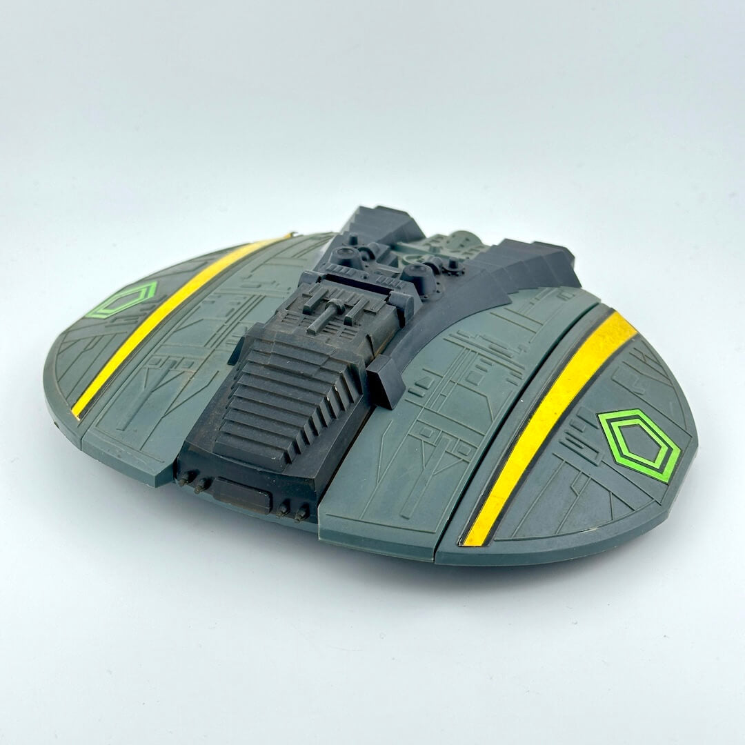 Toy spaceship model with green and yellow accents on a light gray background