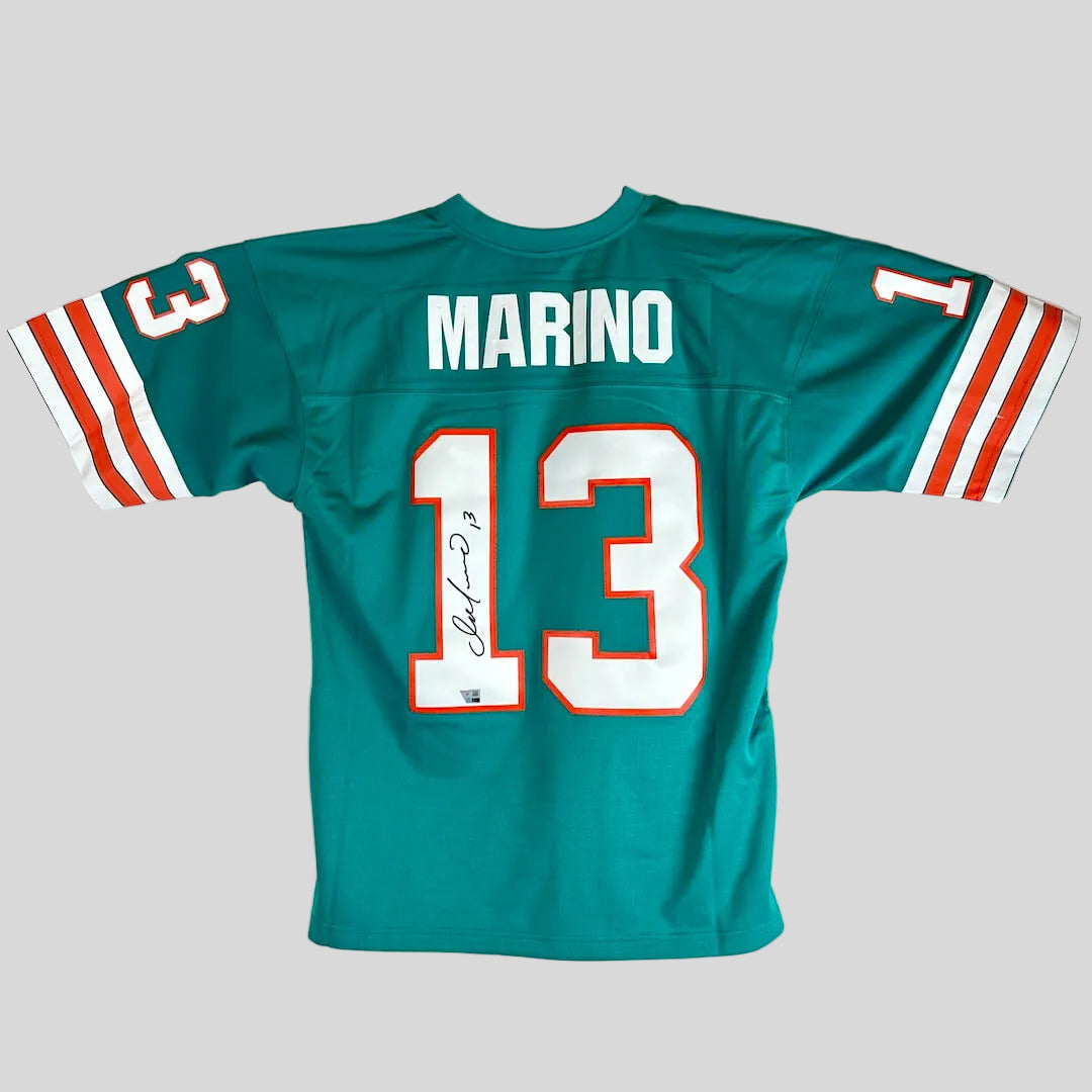 A teal Miami Dolphins football jersey laid flat, showing the back with 'MARINO' & the number '13' in white with orange outlines.