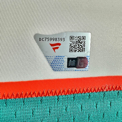 Close-up of a white woven fabric surface with a sticker tag showing a red stylized logo, & a QR code.