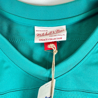 Close-up of a turquoise Mitchell & Ness Legacy Collection V-neck shirt showing the inner neck label and hangtag.
