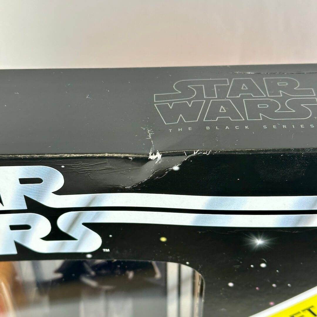 Close-up of a Star Wars The Black Series collectible figure box, showing dent to center of top edge. 
