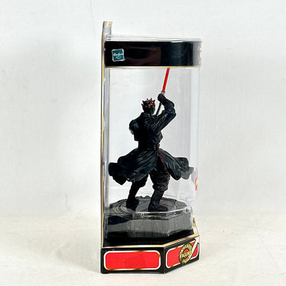 Black figurine with a red lightsaber in a clear display case on a white background