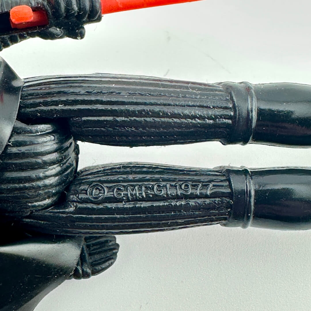 Close-up of a black articulated plastic action figure limb with a stamped copyright mark reading '© GMFGI 1977'