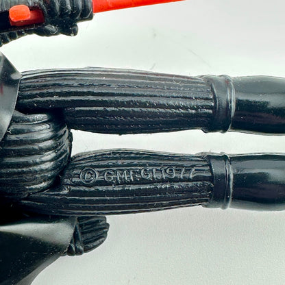 Close-up of a black articulated plastic action figure limb with a stamped copyright mark reading '© GMFGI 1977'