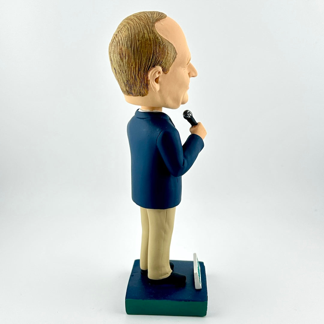 Bobblehead figure of a person in a suit holding a microphone on a white background
