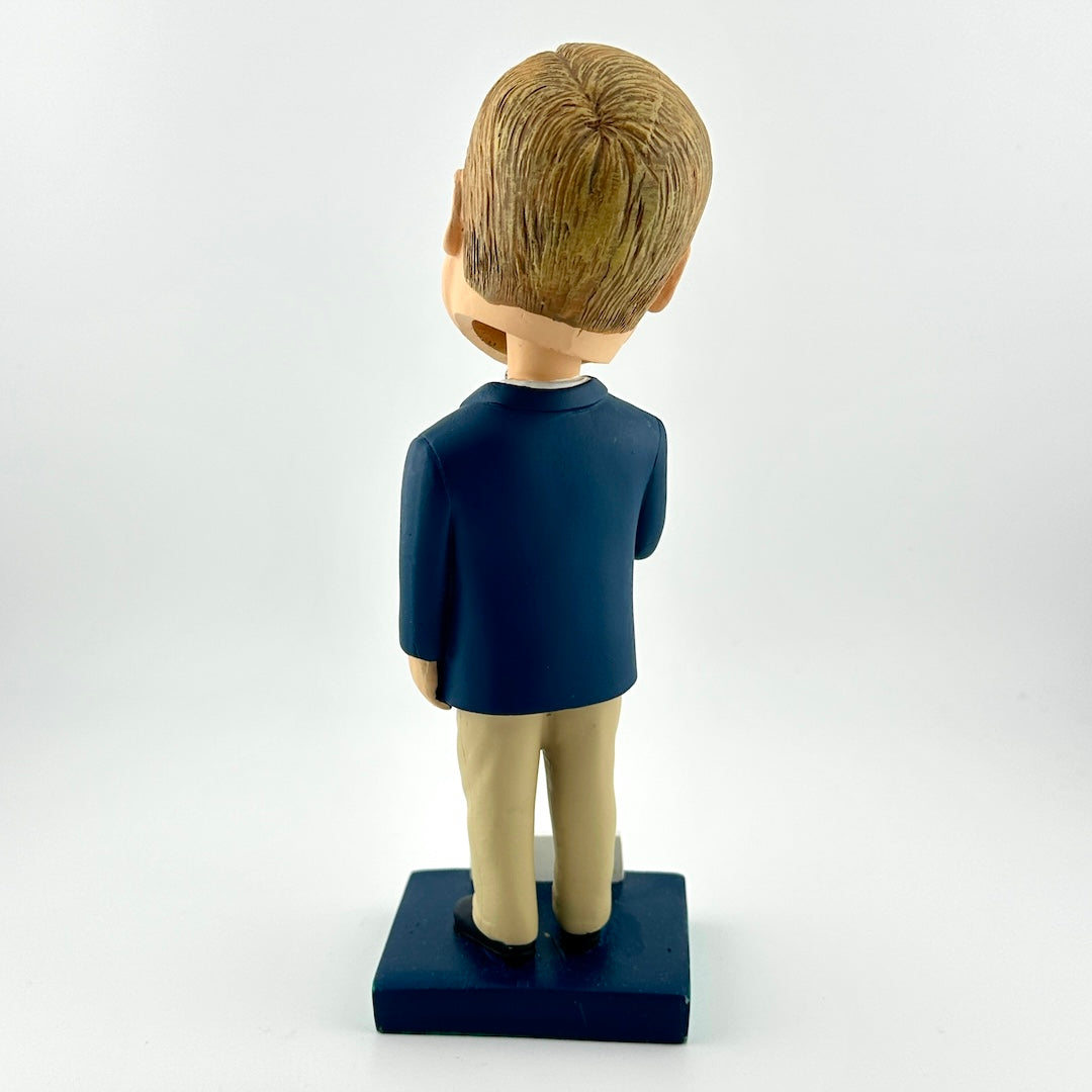 Bobblehead figure of a person wearing a dark blue shirt and beige pants on a white background