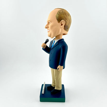 Bobblehead figure of a man in a suit holding a microphone on a white background