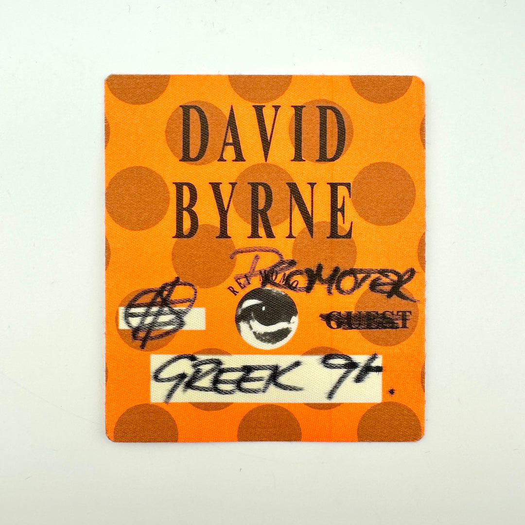 Orange square backstage pass with polka dot background print and black text with artist name and handwritten details. 