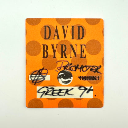 Orange square backstage pass with polka dot background print and black text with artist name and handwritten details. 