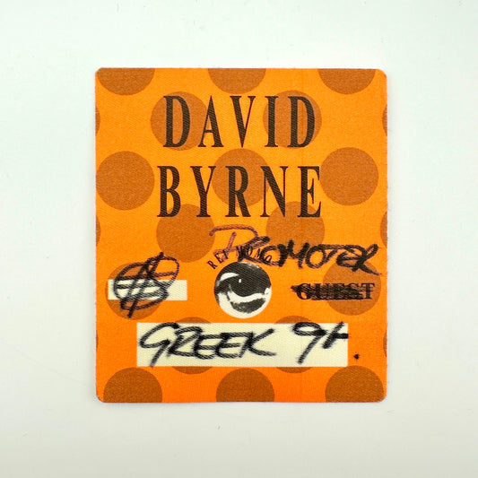 Orange square backstage pass with polka dot background print and black text with artist name and handwritten details. 