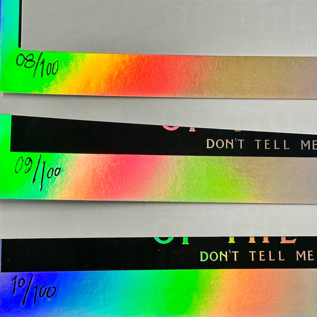Three posters laid out so the poster numbering is visible as well as the highly reflective rainbow foil quality of the paper. 