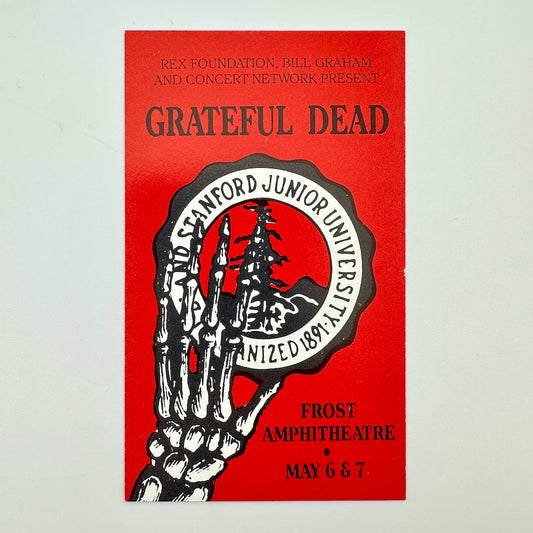 Card for "GRATEFUL DEAD" show with red background and skeletal hand holding Stanford emblem. 