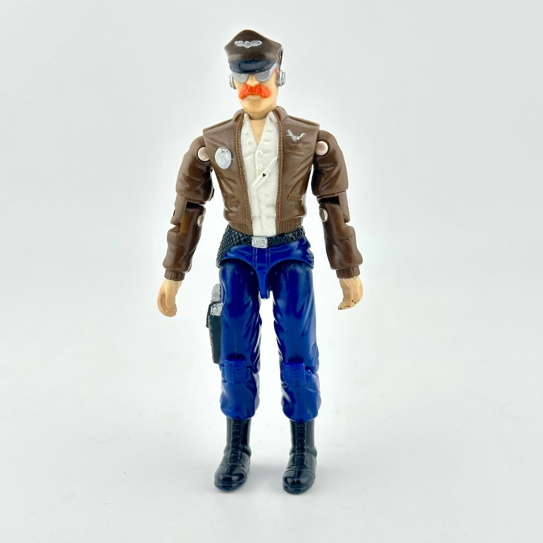GI Joe action figure in blue pants, brown jacket, with aeronautical hat, photographed on white background. 