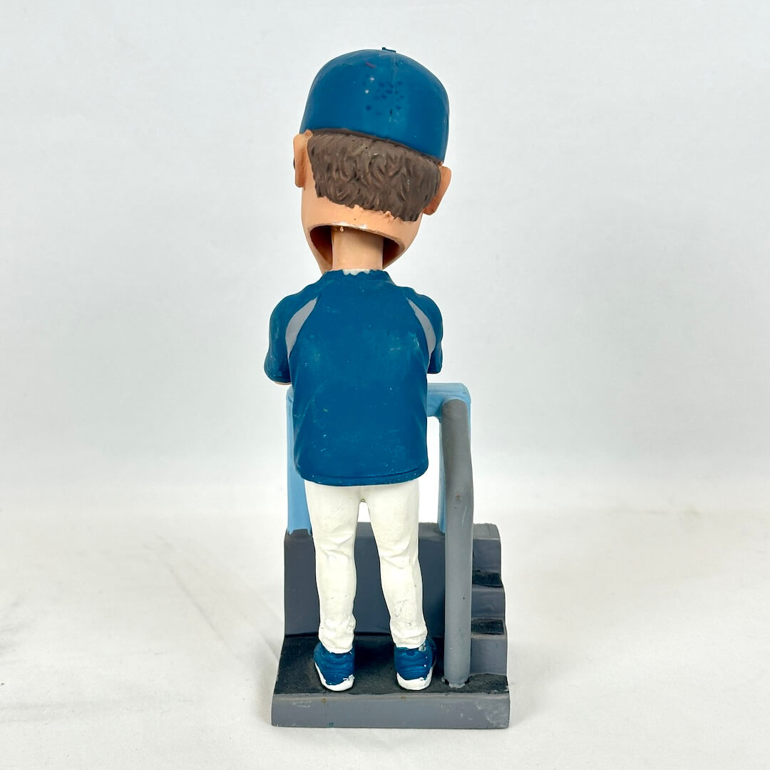 A bobblehead figurine of a baseball player seen from the back, wearing a blue cap, blue jersey, white pants, and blue sneakers.