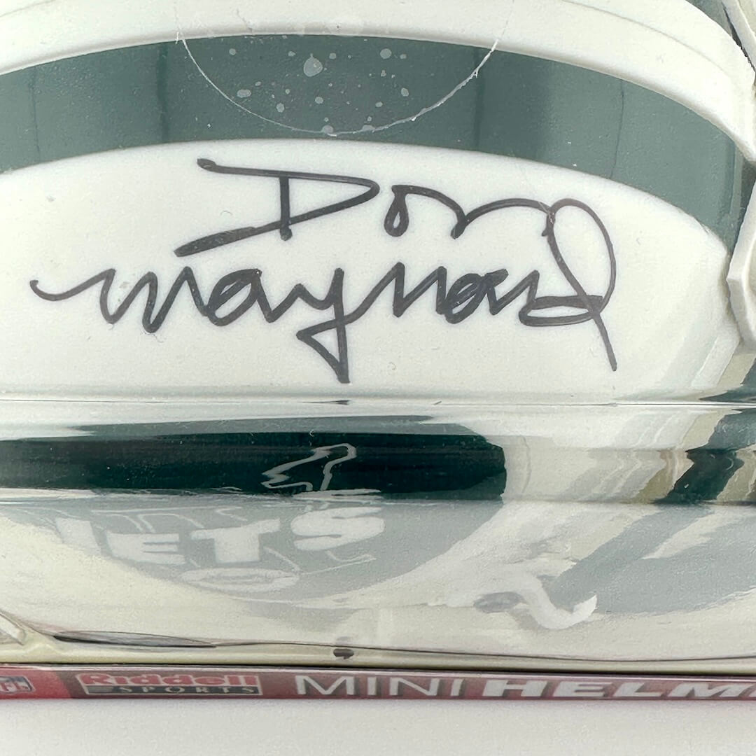 Close-up of a white helmet with a signature on the top, featuring the brand 'Riddell'.