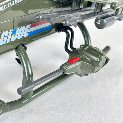 Close-up of gun on side of toy helicopter, other gray missiles visible, on white background. 