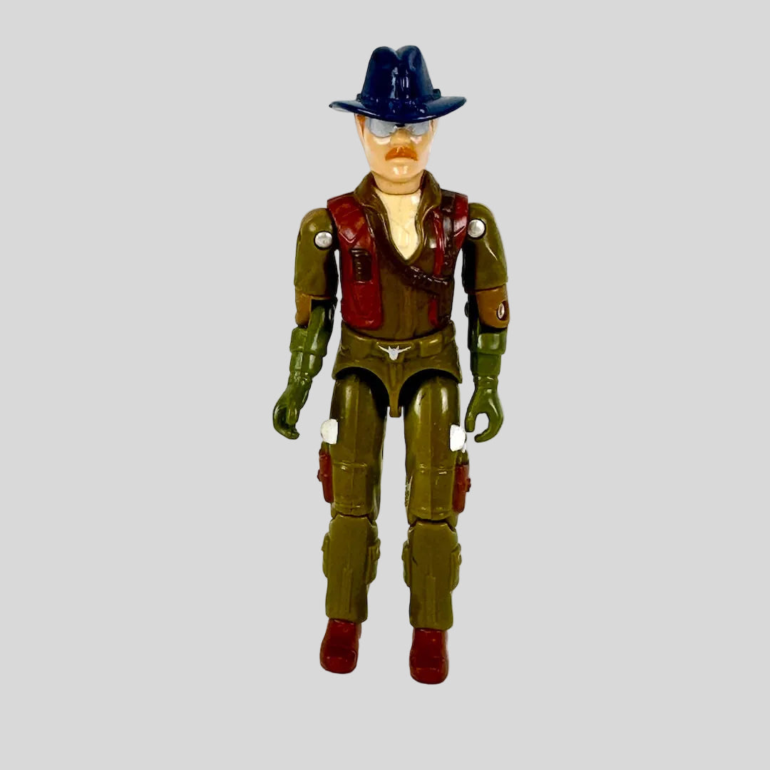 A vintage plastic action figure of a man wearing a dark blue hat, brown vest, olive green pants, and red boots.