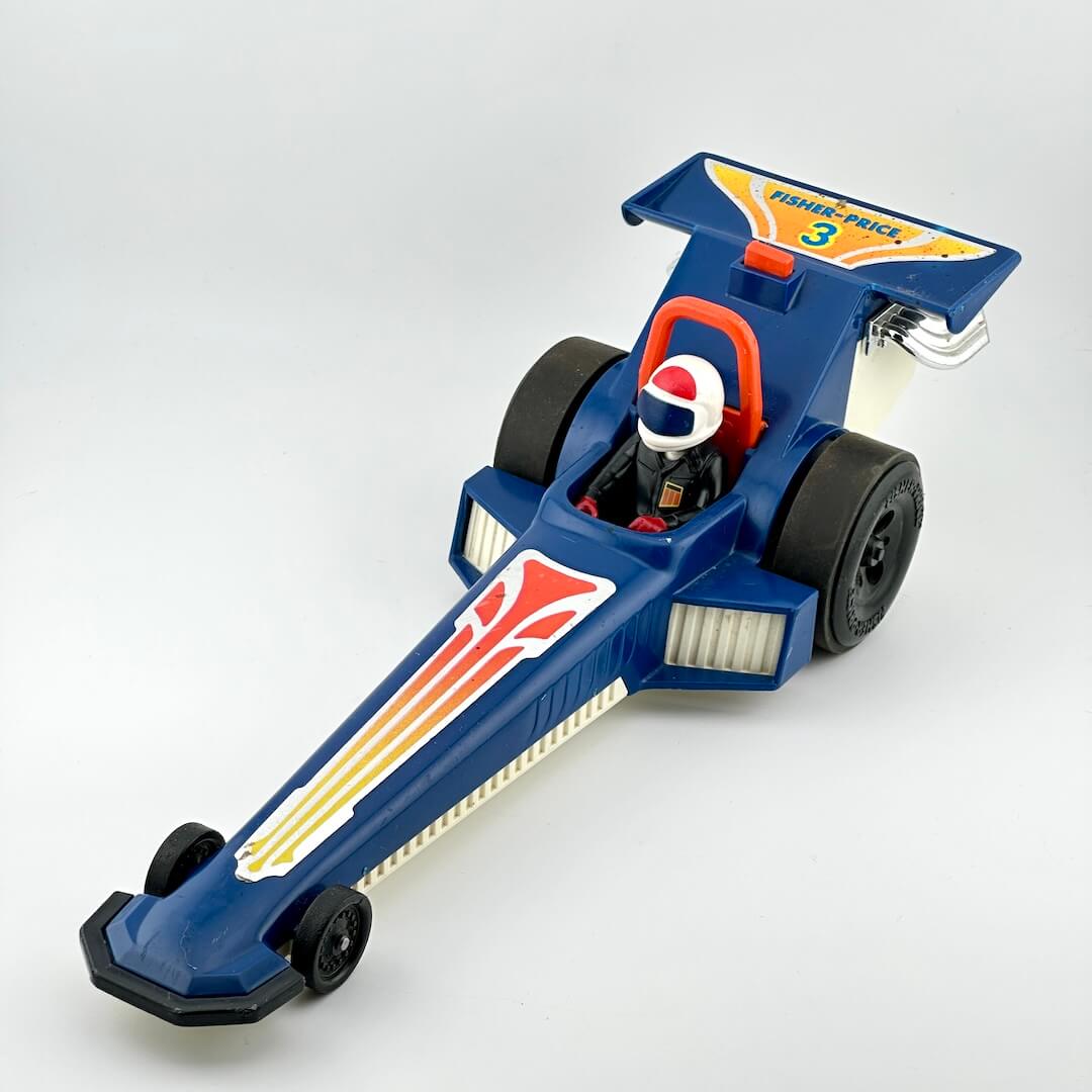 A vintage blue toy drag racer with red, yellow, and white graphics, featuring a driver figure inside.