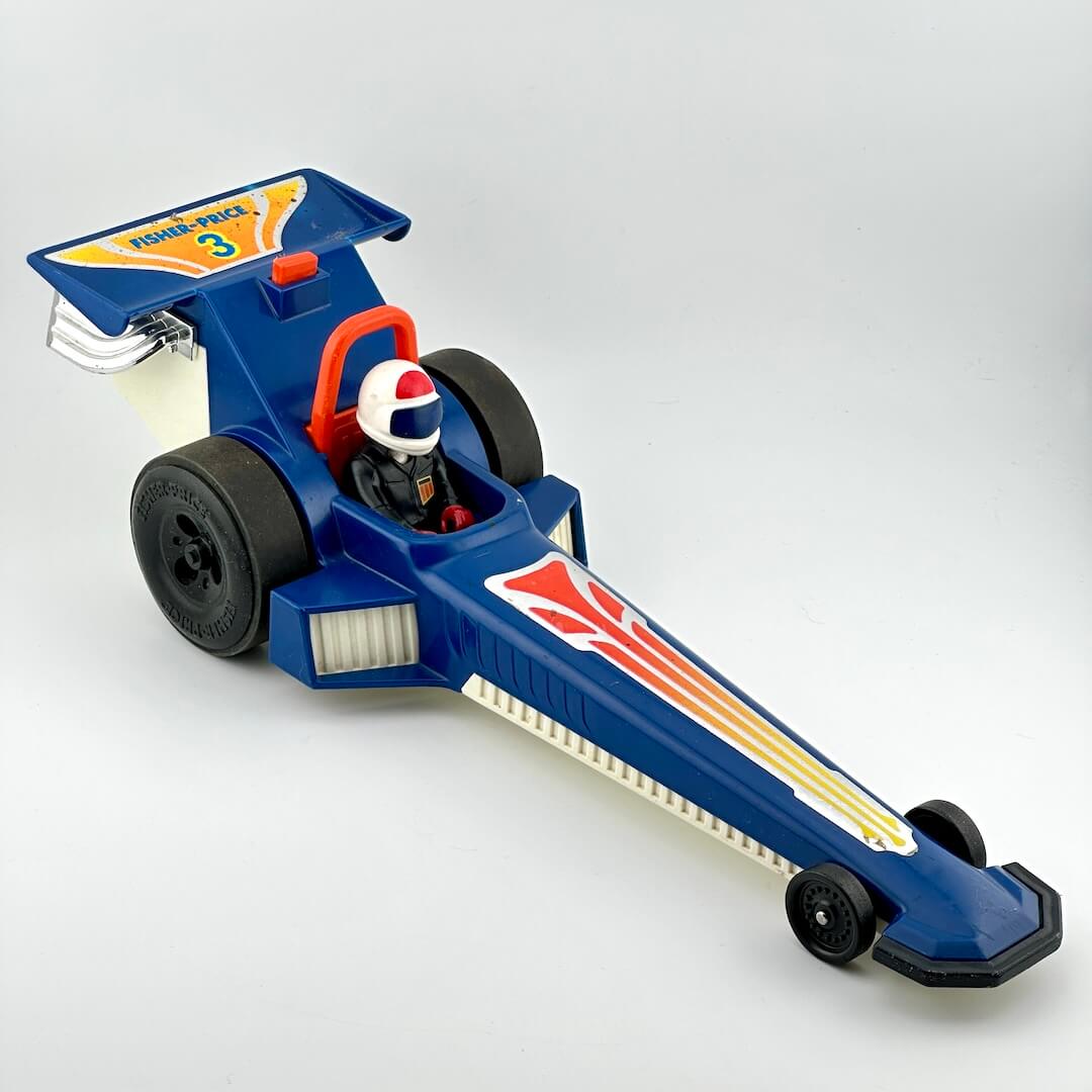 A vintage blue toy drag racer with red, yellow, and white graphics, featuring a driver figure inside.