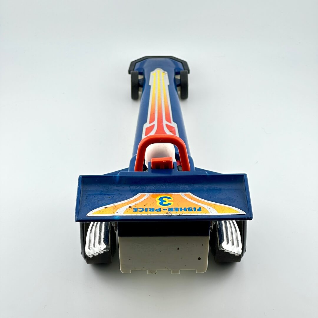 A vintage blue toy drag racer with red, yellow, and white graphics, featuring a driver figure inside.