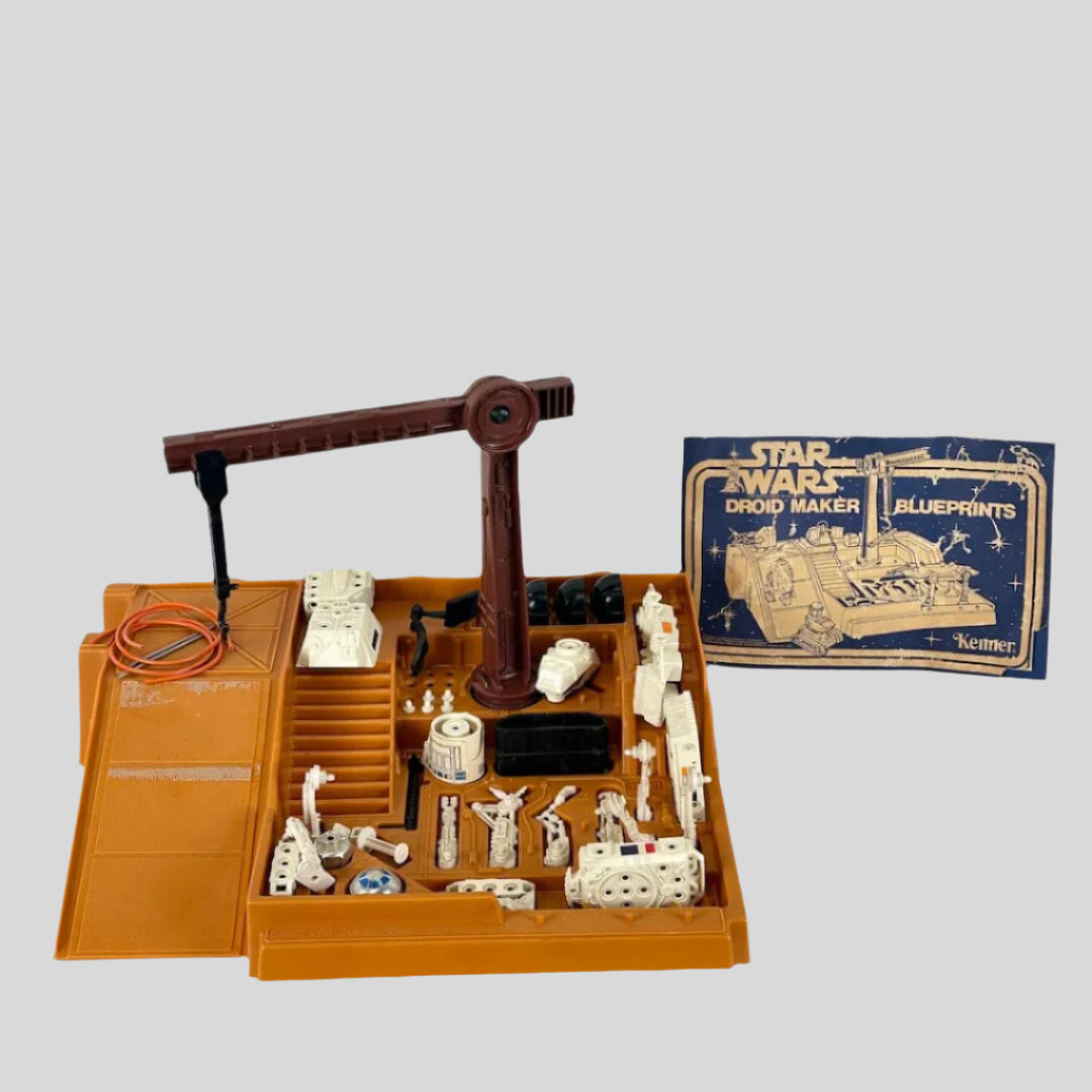 Toy droid maker set with various components and a blueprints book on a white background